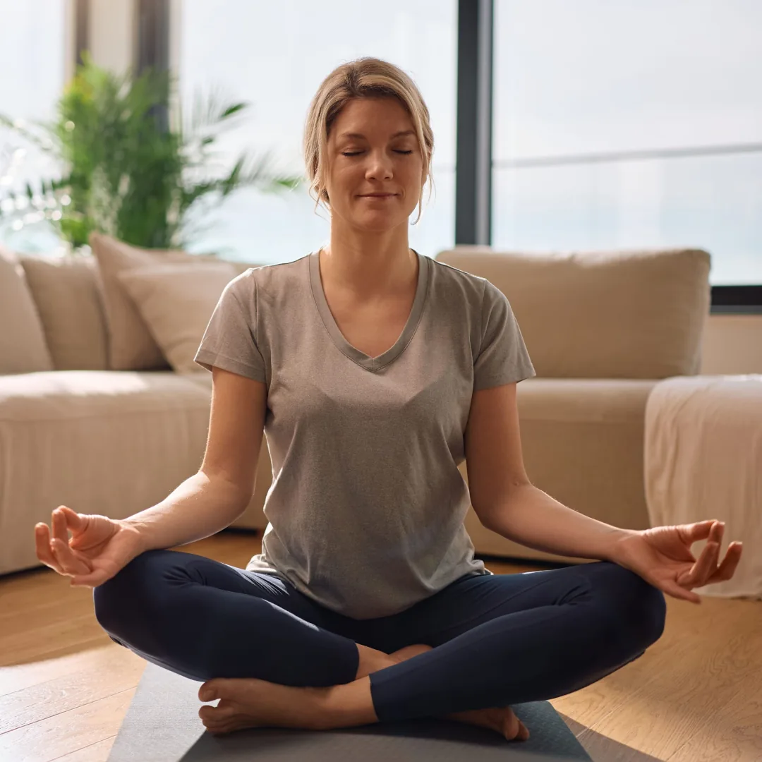 Boydan boya PVC pencerelerin önünde, gün ışığı alan sakin bir salonda meditasyon yapan kadın